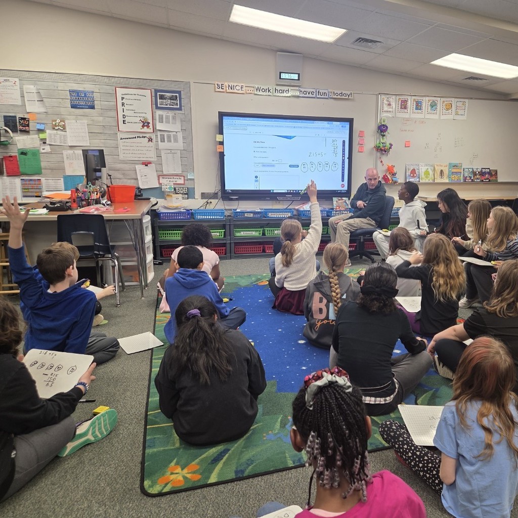 students at carpet, teacher at board