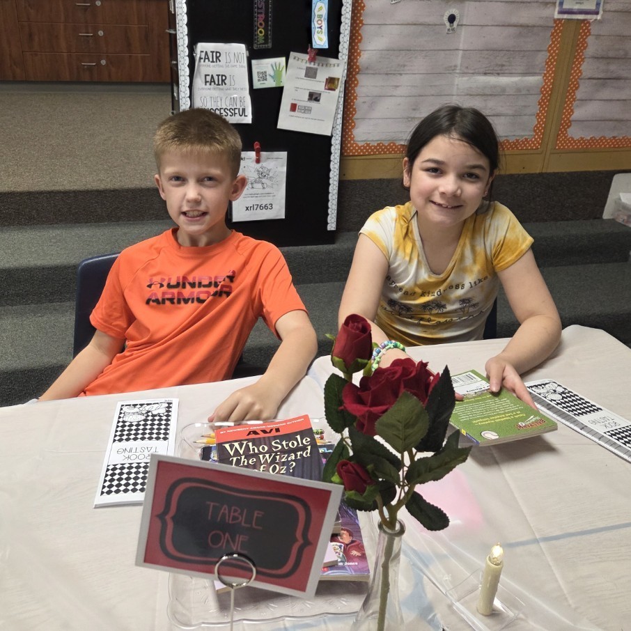 two students at desks set with candle roses, table sign, etc
