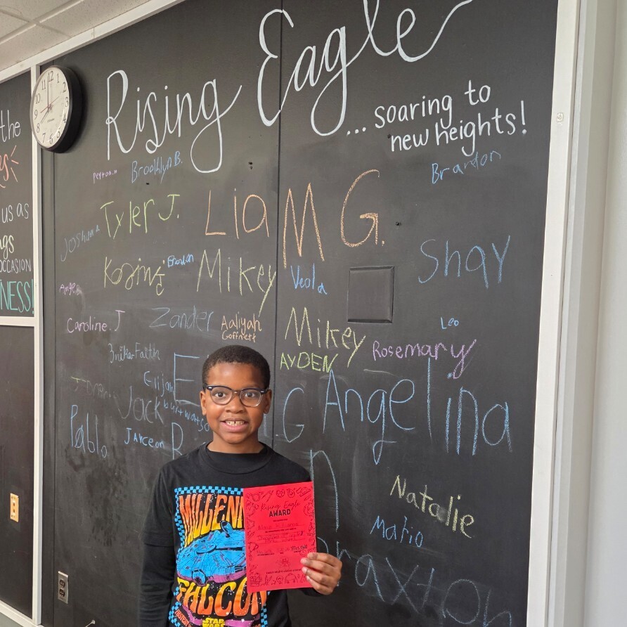 student with certificate in front of walk with names signed in chalk