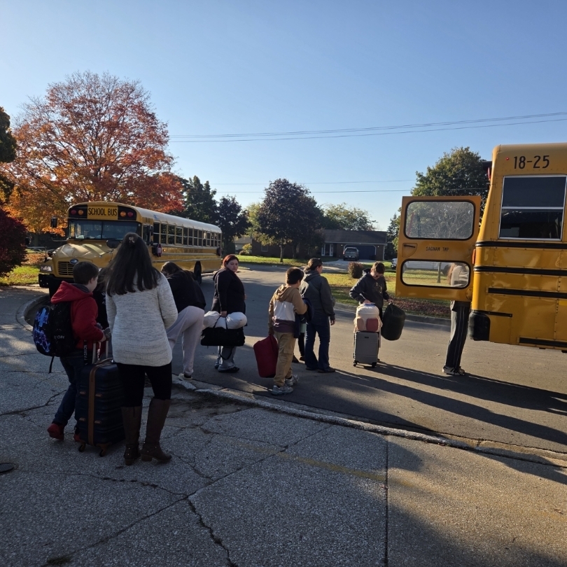 students and parents load luggage on bus