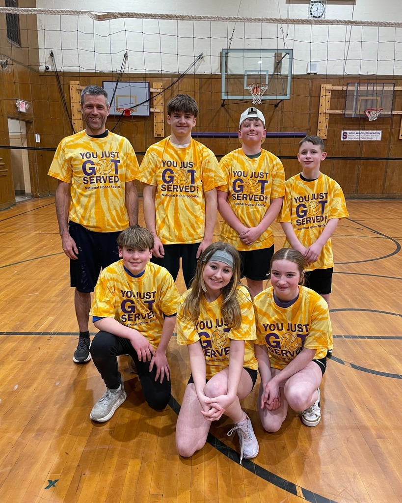 group of students wearing yellow tie-dye shirts posing on volleyball court