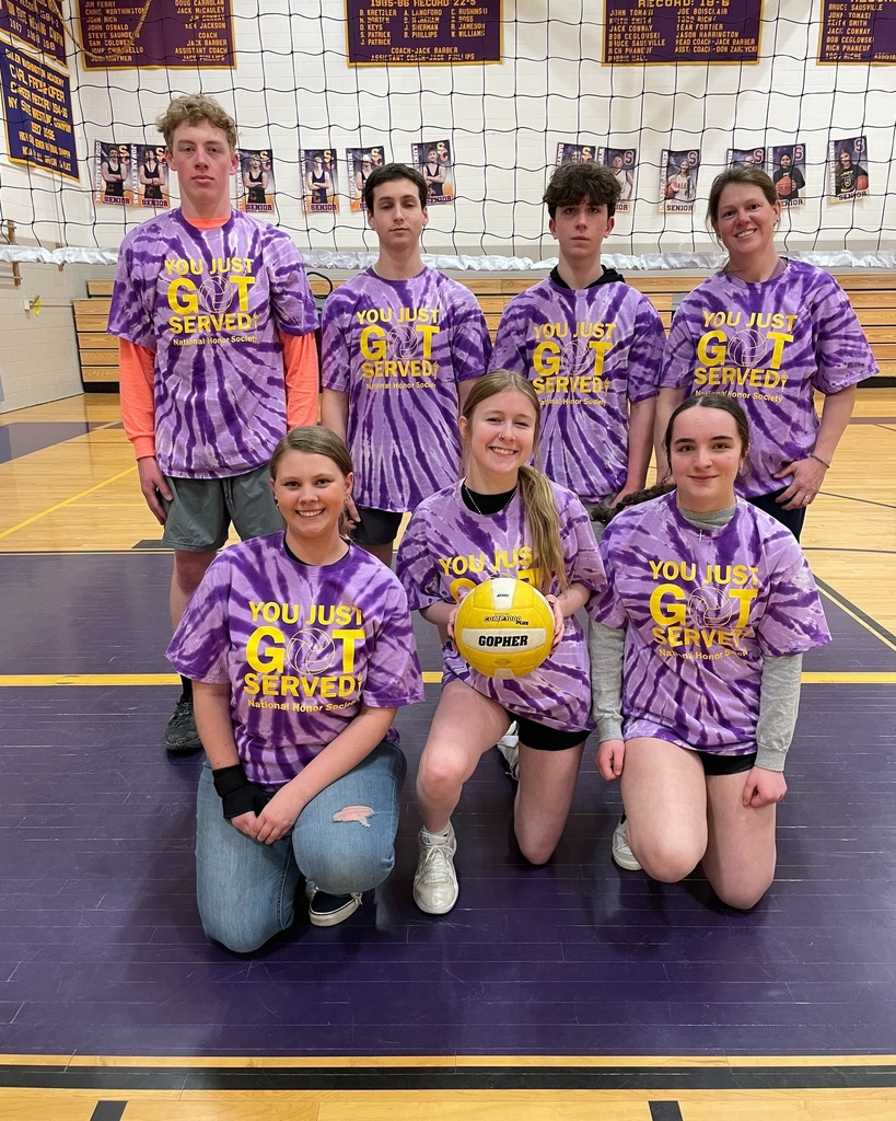 group of students wearing purple tie-dye shirts posing on volleyball court