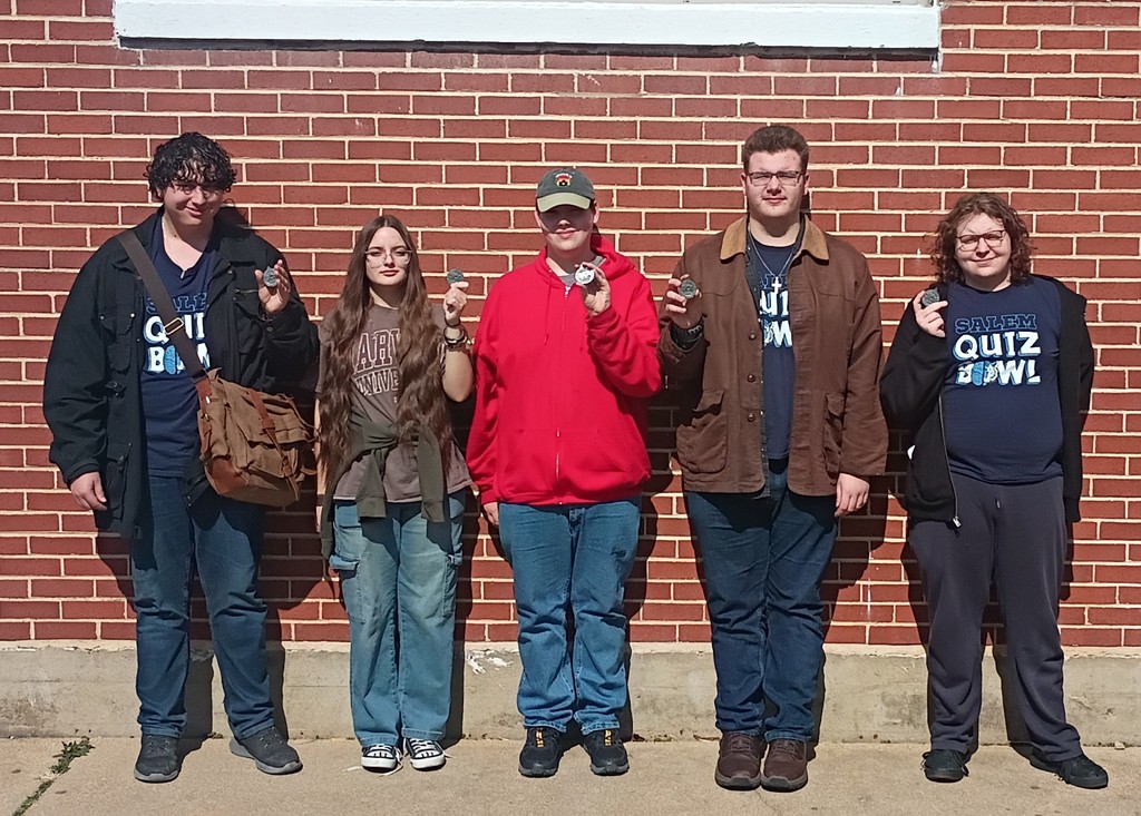 A group of high school students in front of a brick wall holding medals