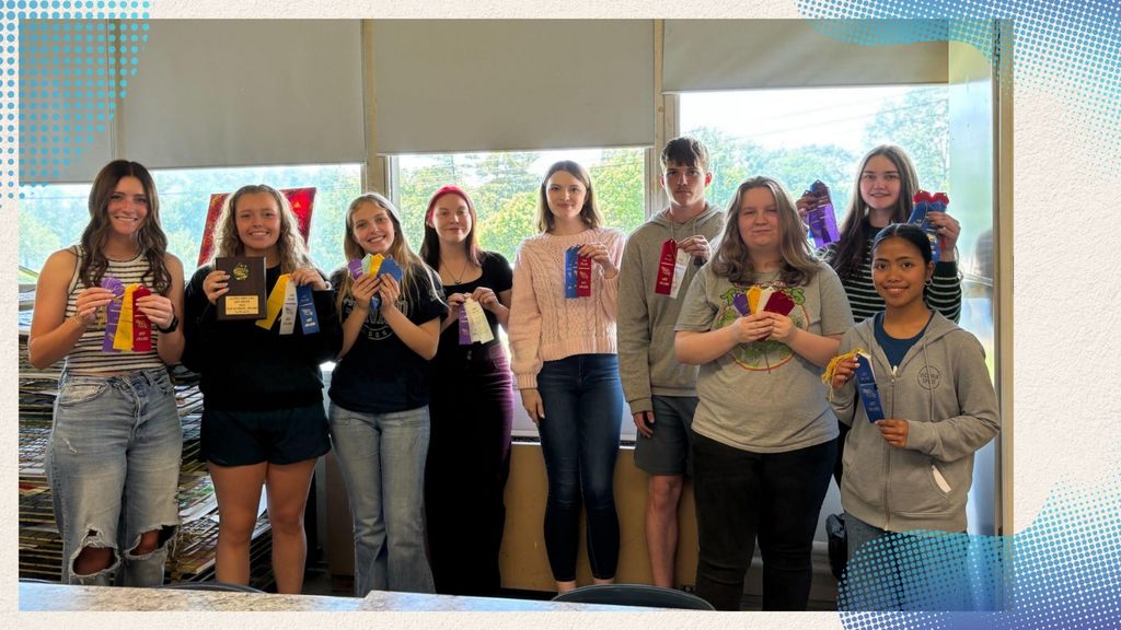 A group of nine people, mostly young women, are standing in front of a window, each holding award ribbons or a trophy.