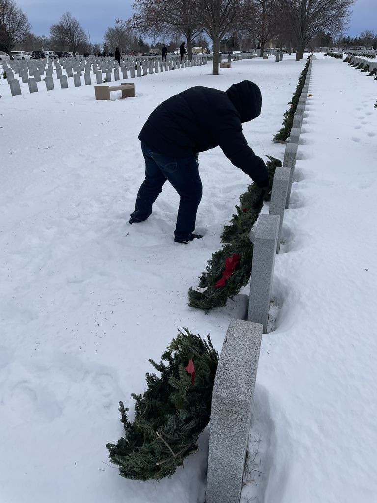 student placing wreath on veteran's grave for Wreath's across america in a snowy graveyard.