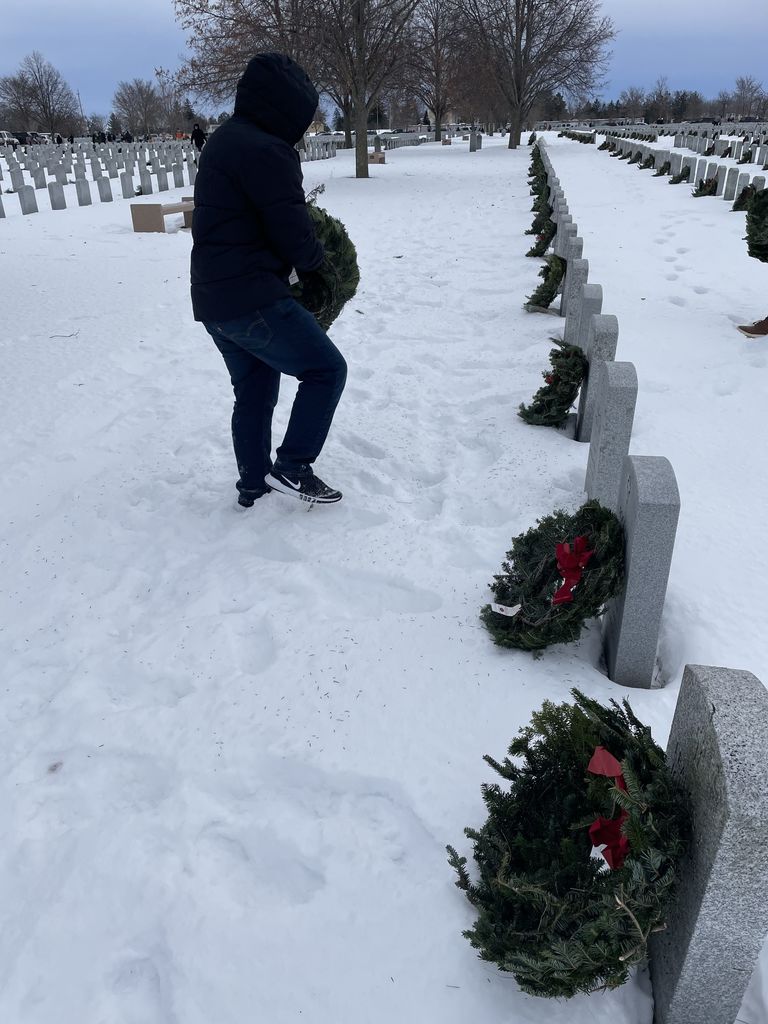 student placing wreath on veteran's grave for Wreath's across america in a snowy graveyard.