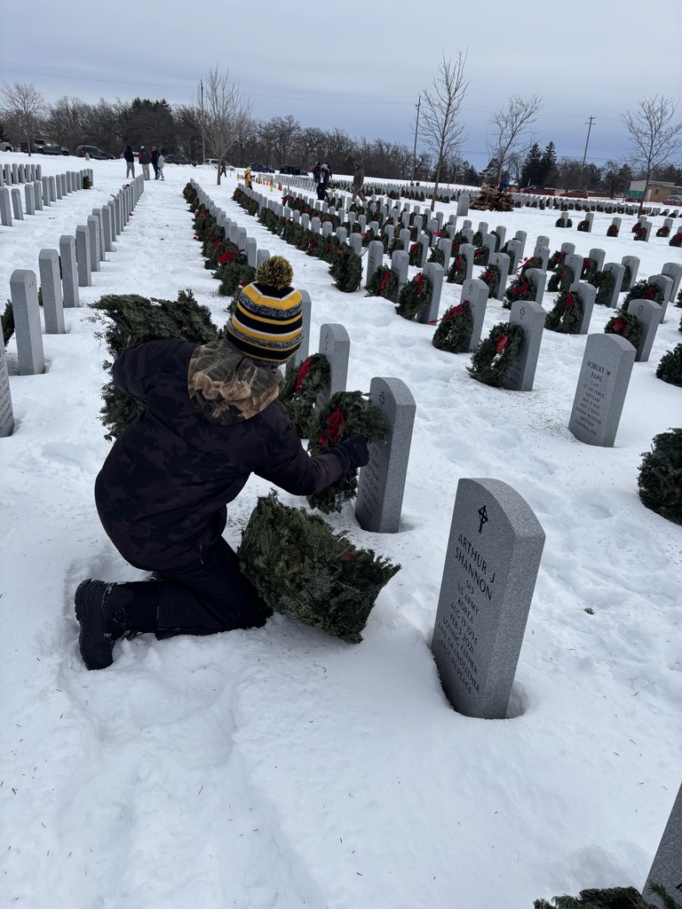 student placing wreath on veteran's grave for Wreath's across america in a snowy graveyard.