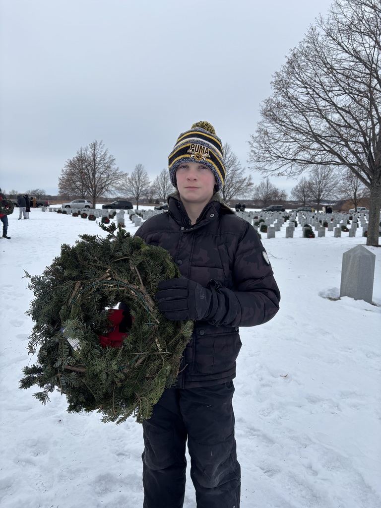 student placing wreath on veteran's grave for Wreath's across america in a snowy graveyard.