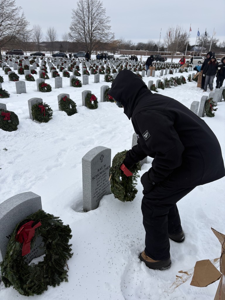 student placing wreath on veteran's grave for Wreath's across america in a snowy graveyard.