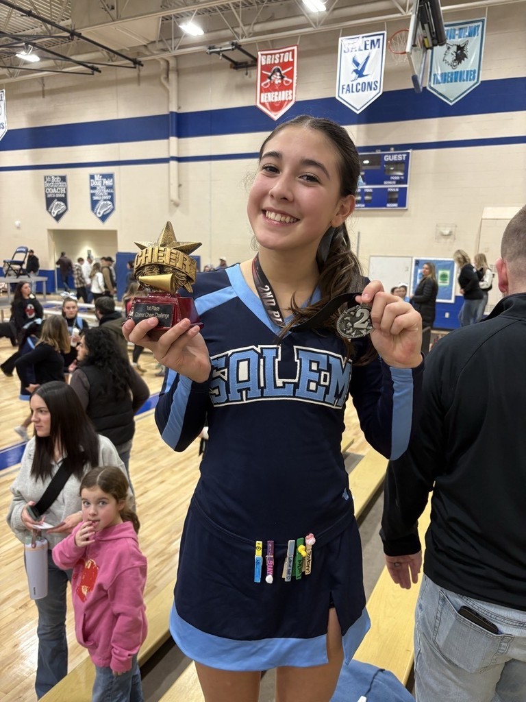 Close-up of a happy Salem student-athlete proudly displaying her cheerleading trophy and a second-place medal in a crowded gym.