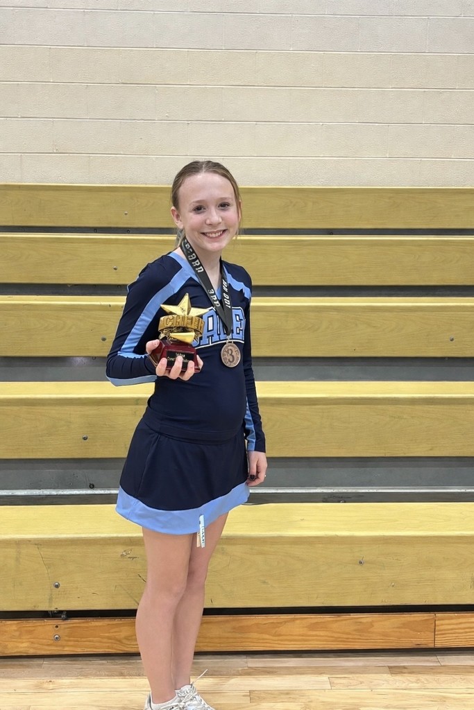 A smiling Salem cheerleader in a navy and light blue uniform holding a star-shaped 3rd place trophy while standing in front of gymnasium bleachers.
