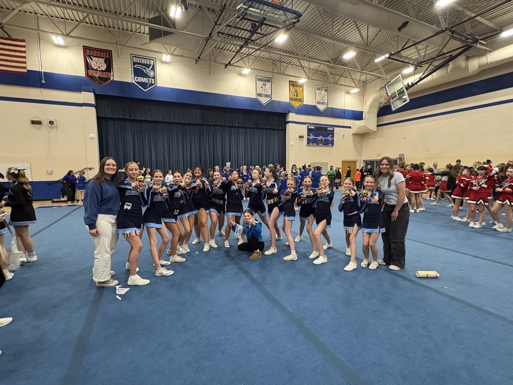 Large group of Salem cheerleaders posing together on a blue mat in a gymnasium, each holding up their individual trophies.
