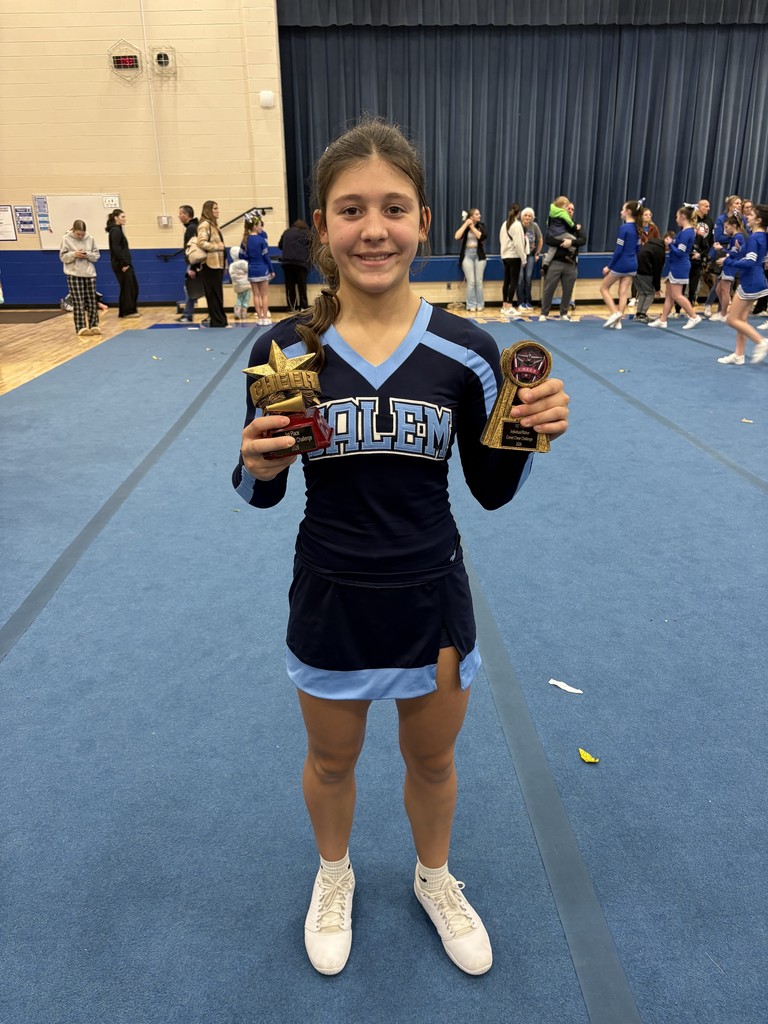 A smiling Salem cheerleader in a navy and light blue uniform holding a star-shaped 1st place trophy while standing in front of gymnasium bleachers.