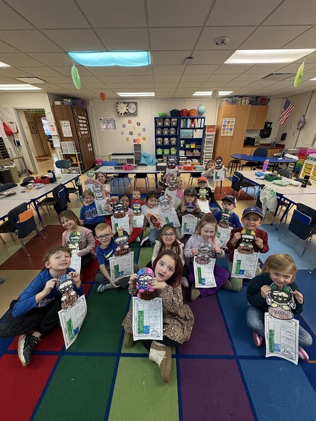 Students sitting on a colorful rug in a classroom, showing off their completed football player paper crafts and data charts.