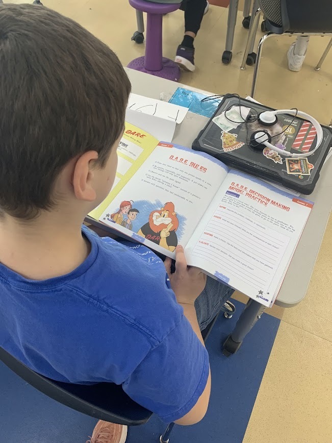 Over-the-shoulder view of a student following along in their D.A.R.E. workbook during a classroom lesson on decision-making.