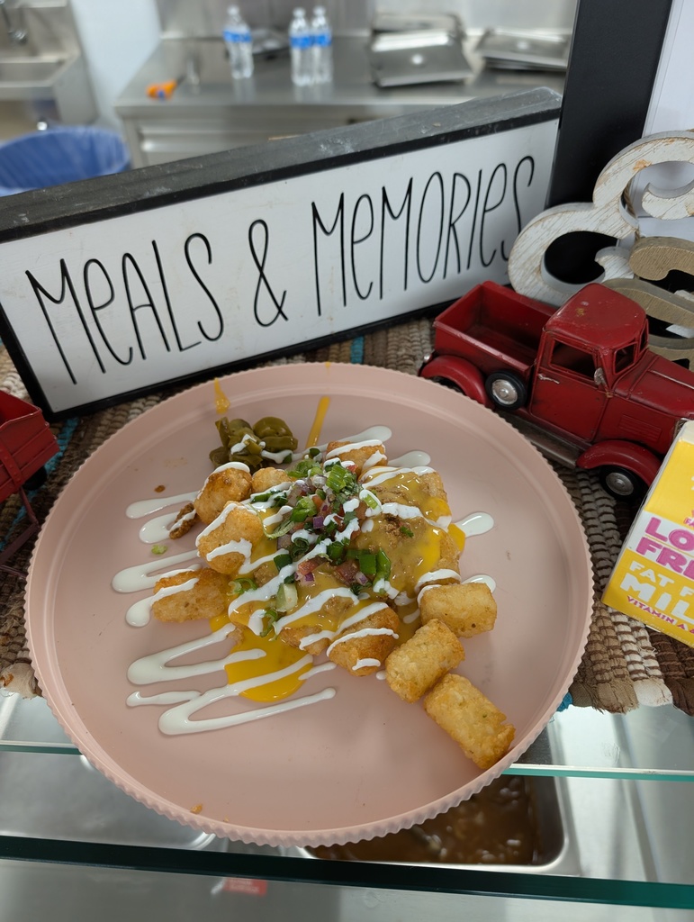 A close-up of a sample plate of "totchos" (tater tot nachos) featuring cheese, meat, jalapeños, and white sauce.
