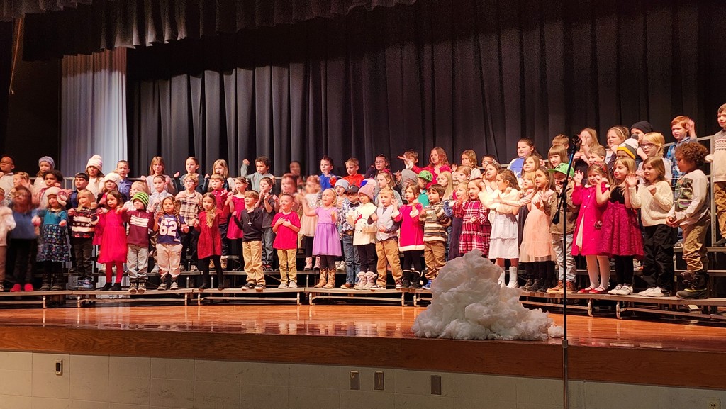 First grade students on risers on a stage signing in a winter themed concert.