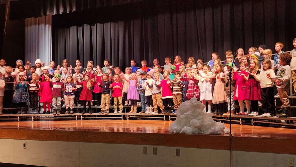 First grade students on risers on a stage signing in a winter themed concert.