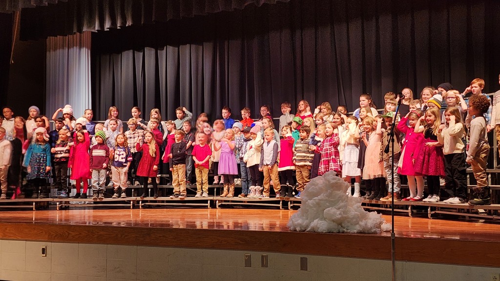 First grade students on risers on a stage signing in a winter themed concert.