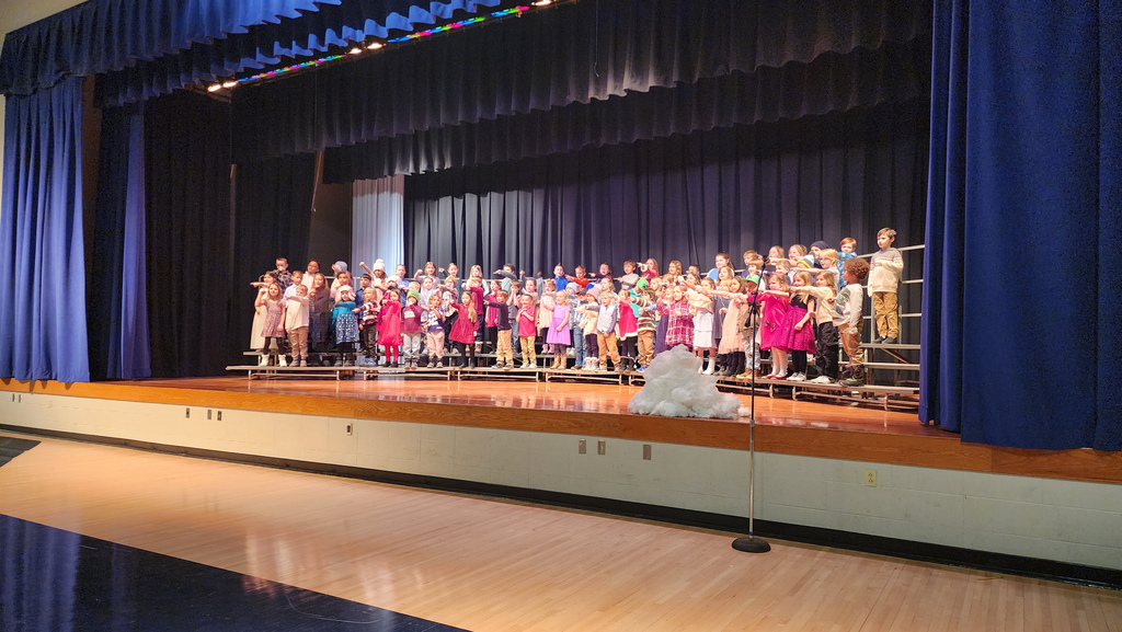First grade students on risers on a stage signing in a winter themed concert.