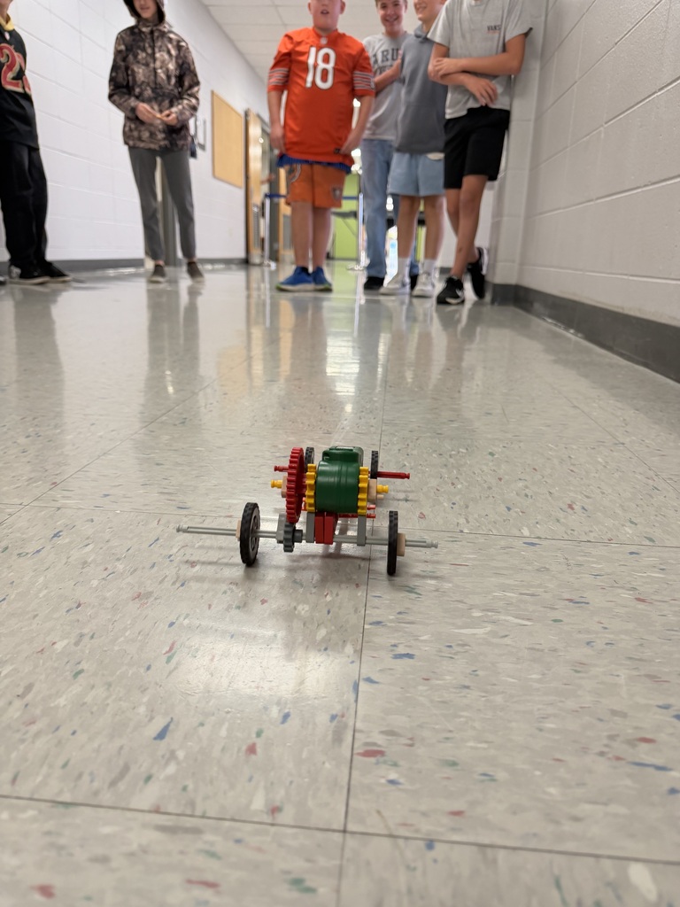 close up of a car racing in a hallway that was created in Robotics with a group of students standing in the background watching