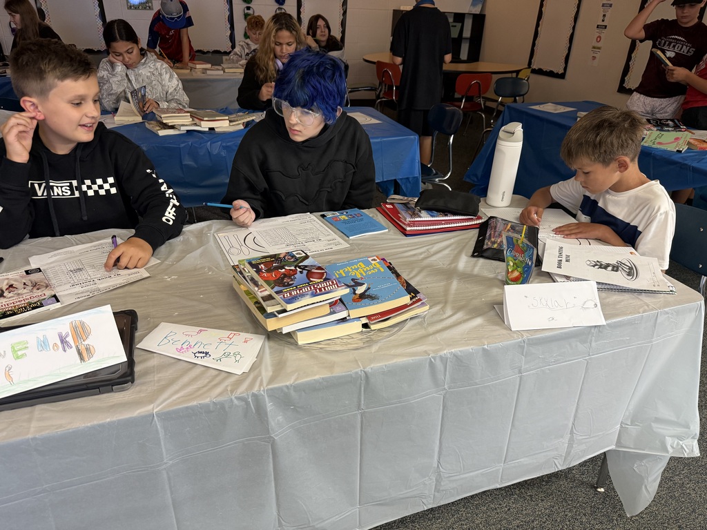 Middle school students sitting around a table with books and worksheets, reading together during a classroom book tasting activity.
