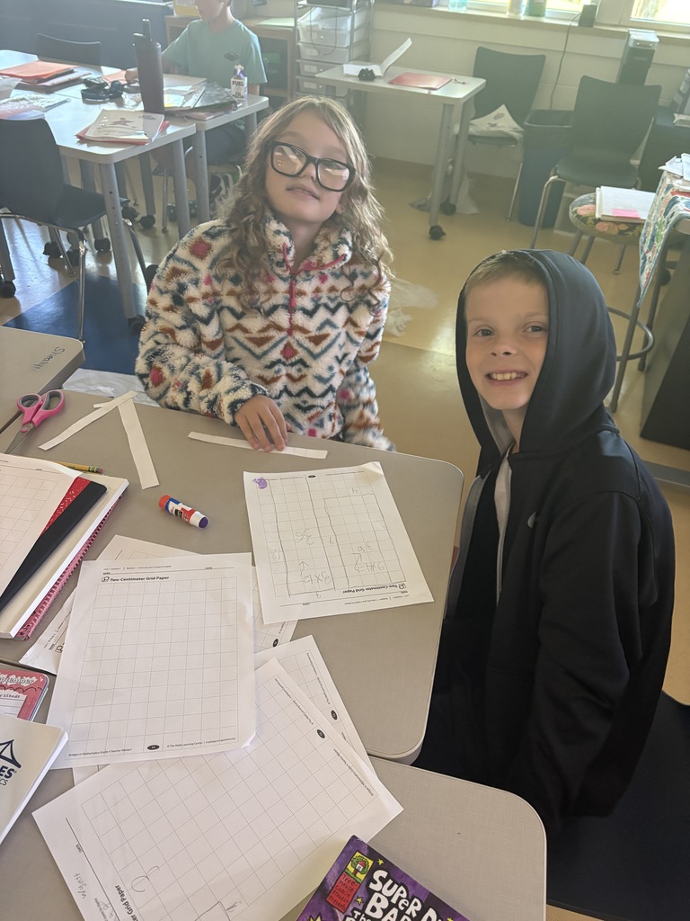 A girl and a boy smiling at their desk while working on math grid paper worksheets.