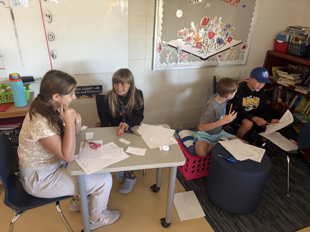 Four elementary students working in small groups at desks and flexible seating areas in a classroom.