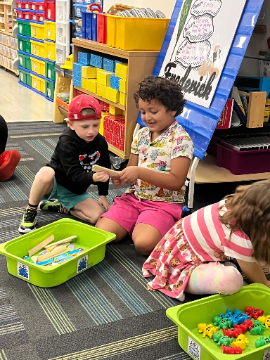 Young students playing together on the classroom floor with wooden craft sticks and plastic counting bears.