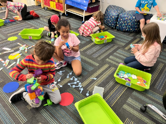 Young elementary students sitting on the classroom floor playing with colorful learning blocks and plastic counting keys.