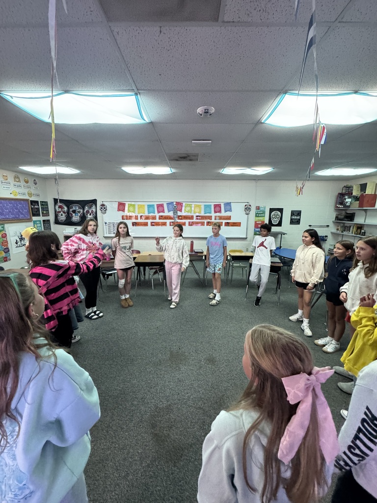 Classroom filled with students standing in a circle while participating in a "Name Speedball" learning game.