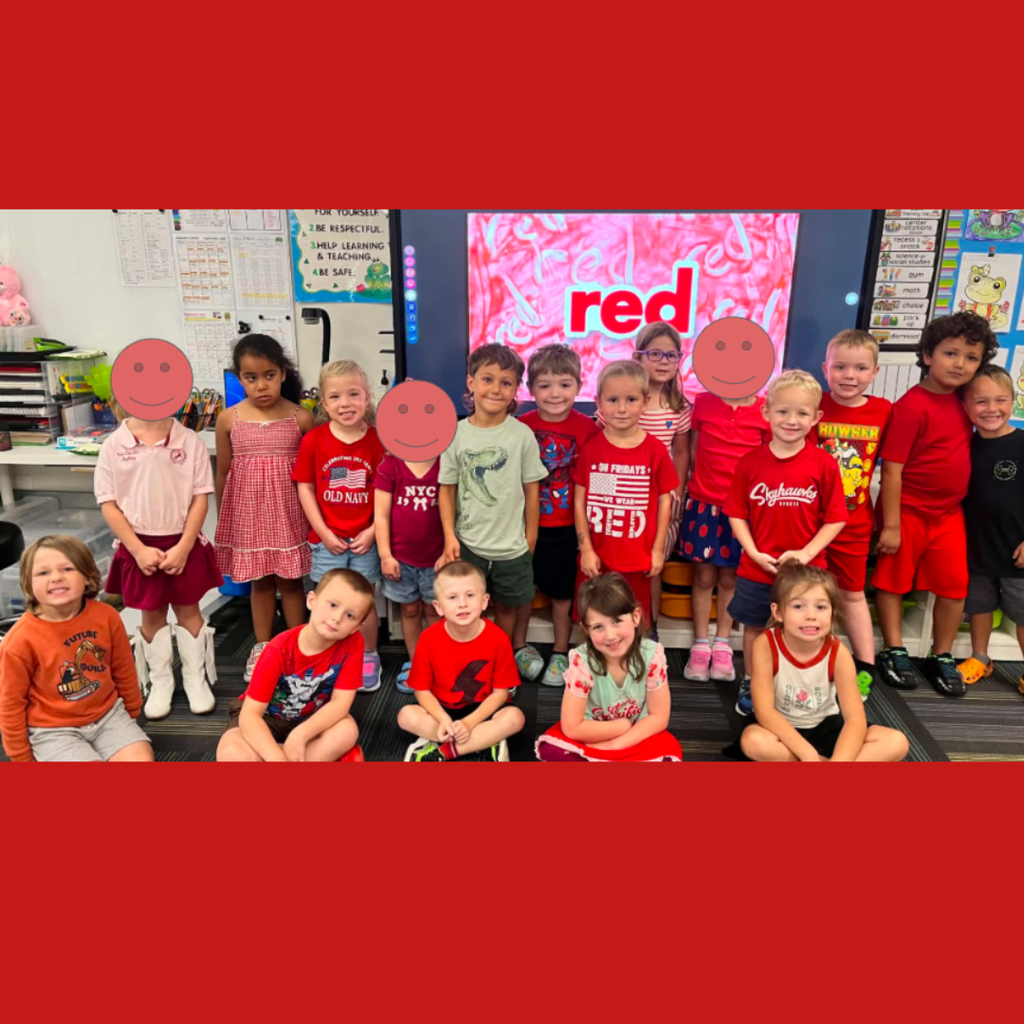 Classroom of elementary students dressed in red clothes posing together in front of a screen reading "red."