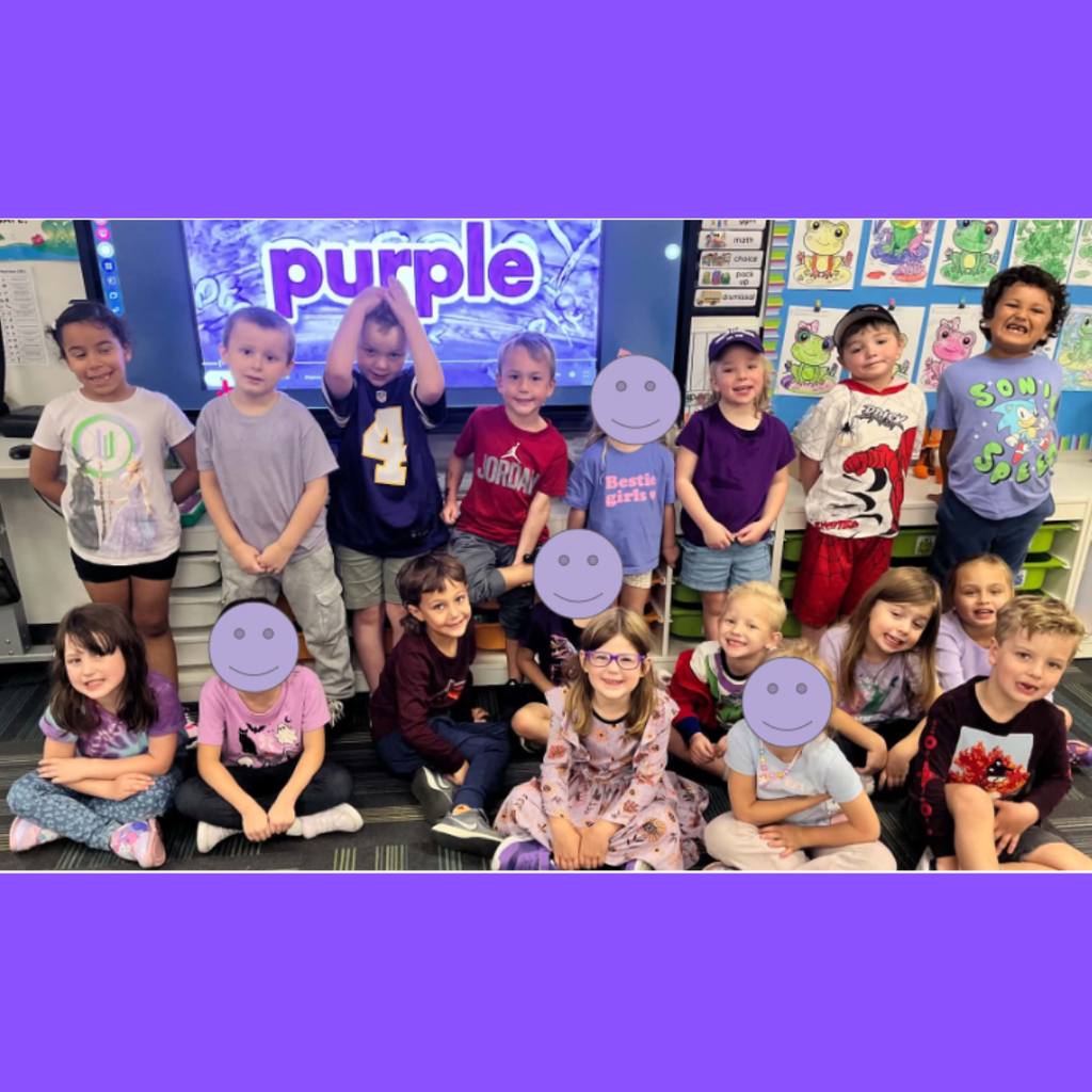 Elementary class wearing purple outfits posing in front of a classroom screen displaying the word "purple."