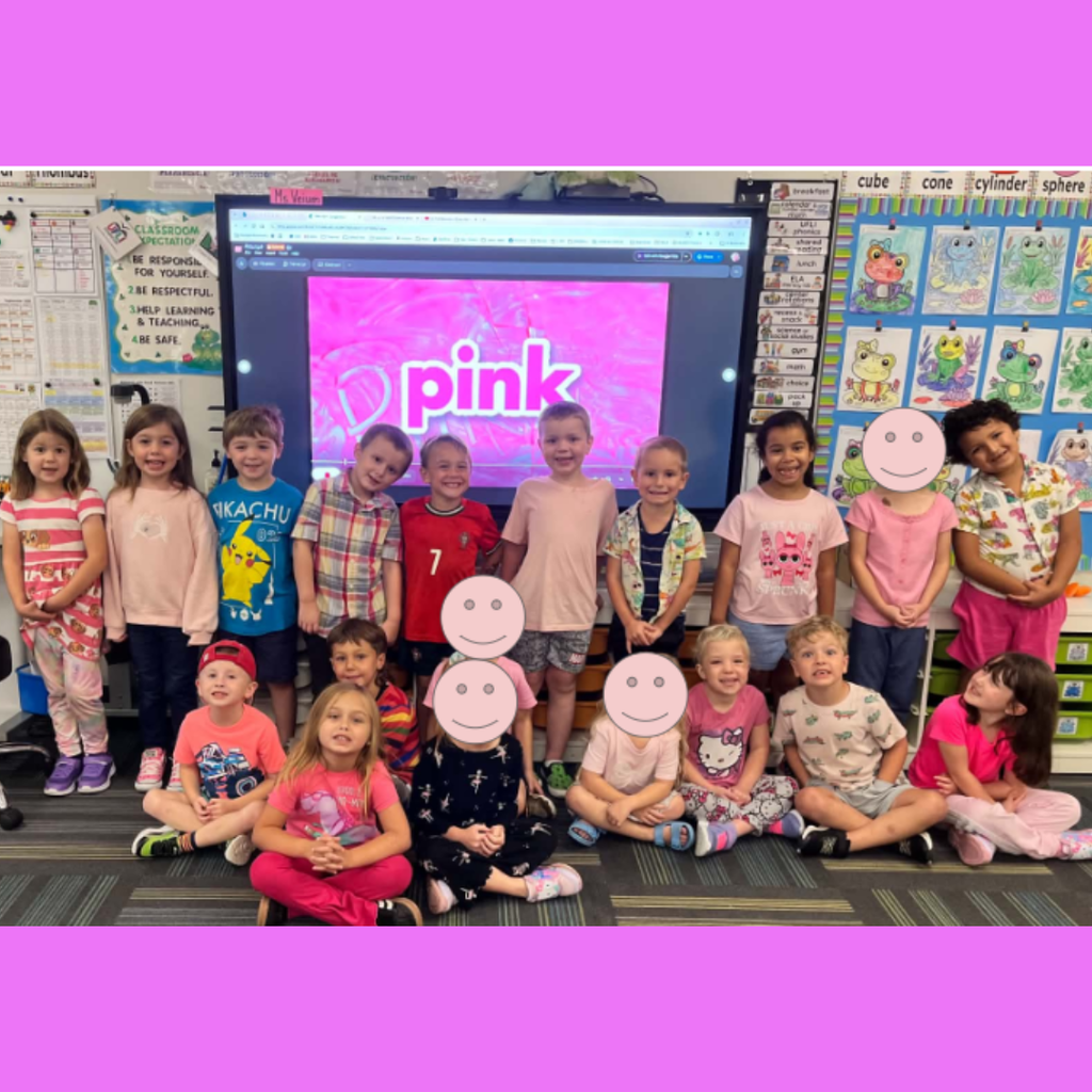 Young students dressed in pink clothing posing together in front of a smart board displaying "pink."