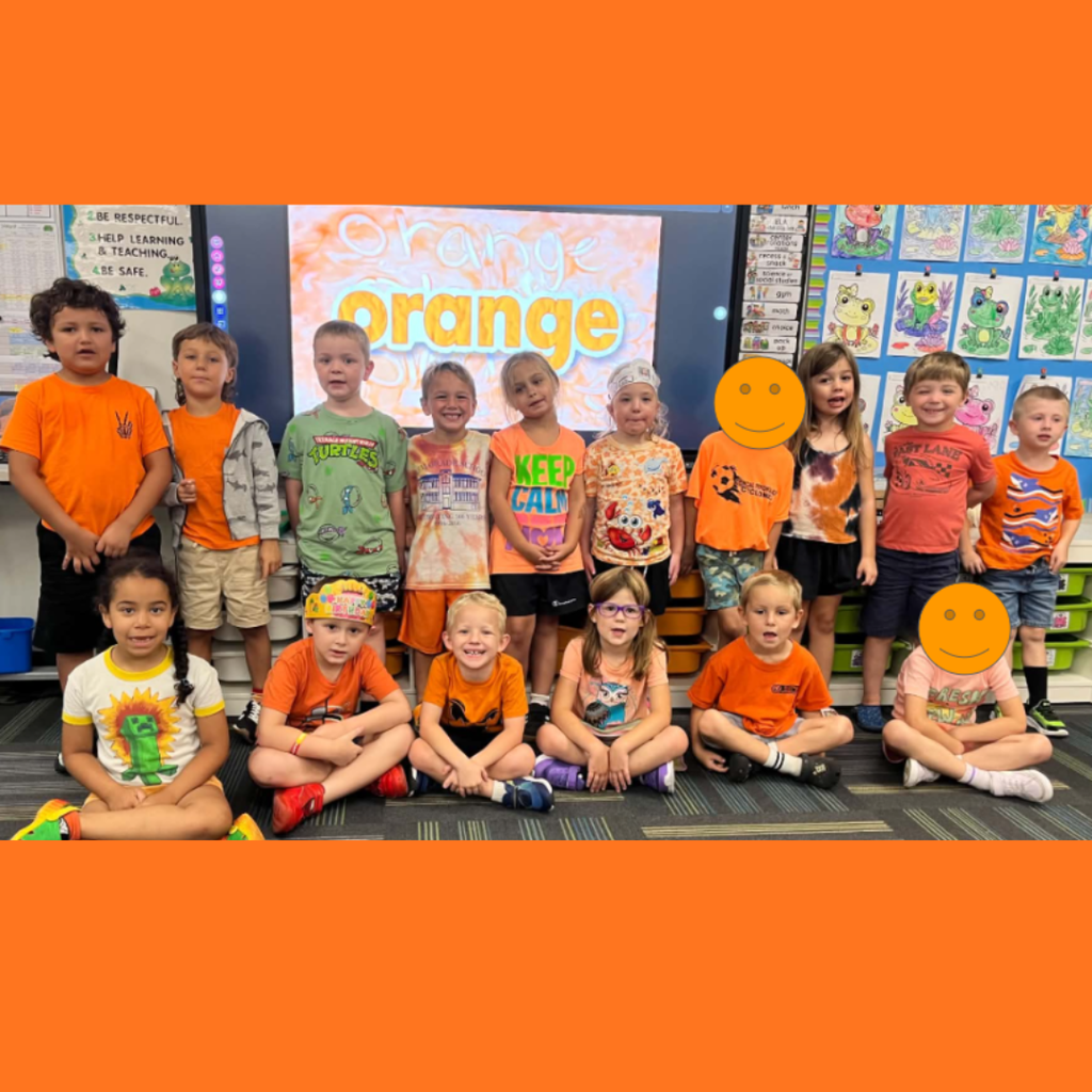 Elementary students wearing orange shirts sitting and standing together in a classroom color-day photo.