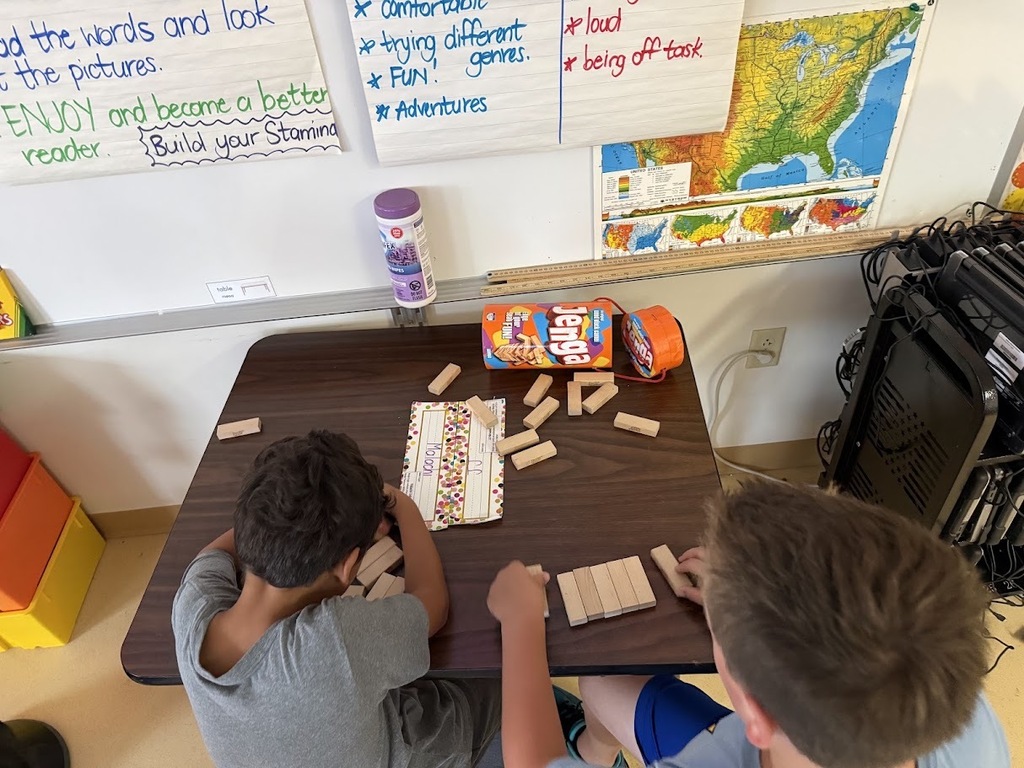 High-angle view of two students sitting at a classroom table building structures with wooden Jenga blocks.