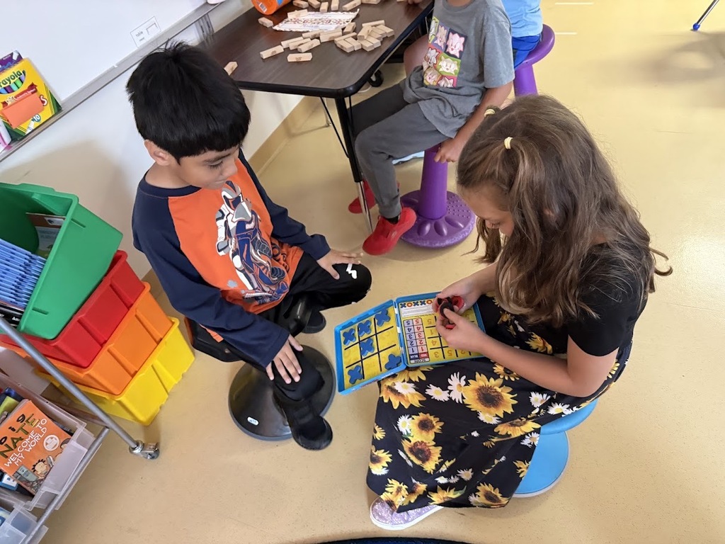 Two elementary students sitting on flexible wobble stools and playing a tabletop game together.