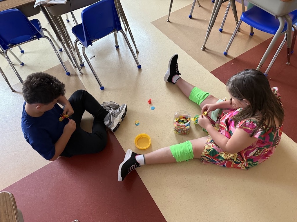 : Two elementary students sitting on the classroom floor playing with colorful building toys together.