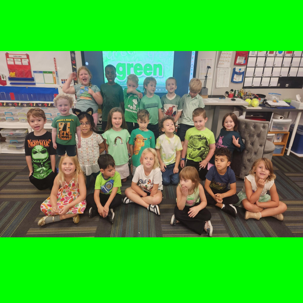 Young students dressed in green outfits gathered for a photo in front of a screen displaying "green."