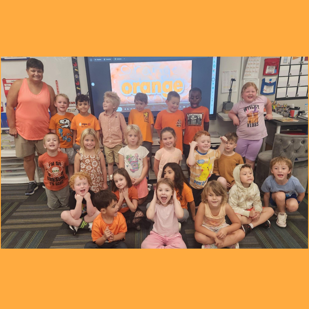 Elementary students wearing orange shirts sitting and standing together in a classroom color-day photo.