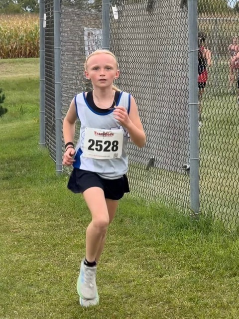 Young girl wearing race bib 2528 and a Salem cross country uniform running along a fence during a meet.