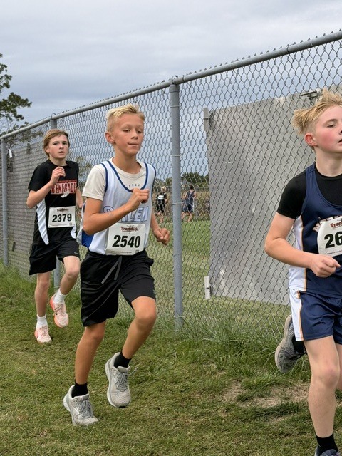 three middle school student athletes running side by side during a cross country race.