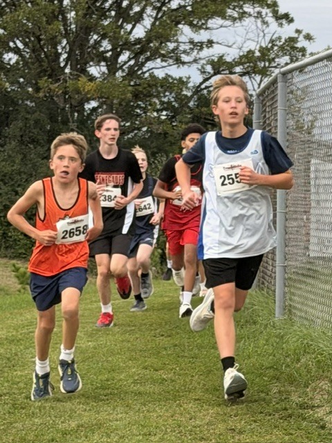 Group of middle school boys running alongside a fence during an outdoor cross country meet.