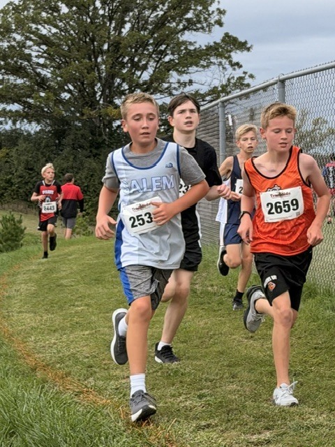 Boy wearing race bib 2531 running alongside another athlete on a grass cross country path.