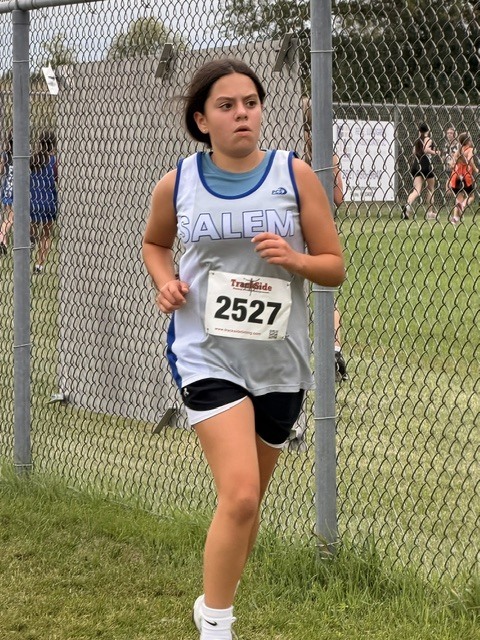 Middle school girl wearing race bib 2527 and a Salem athletic jersey running on a grass course.