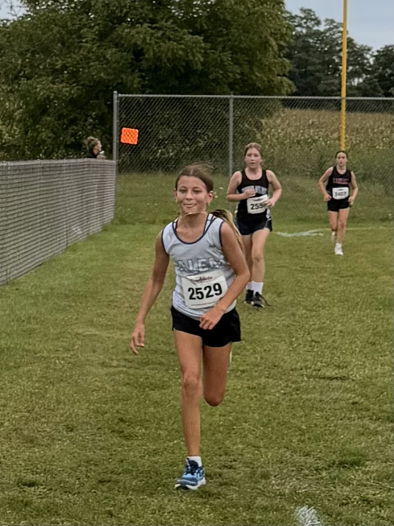 Young runner wearing race bib 2529 leading a group of athletes along a grassy cross country course.