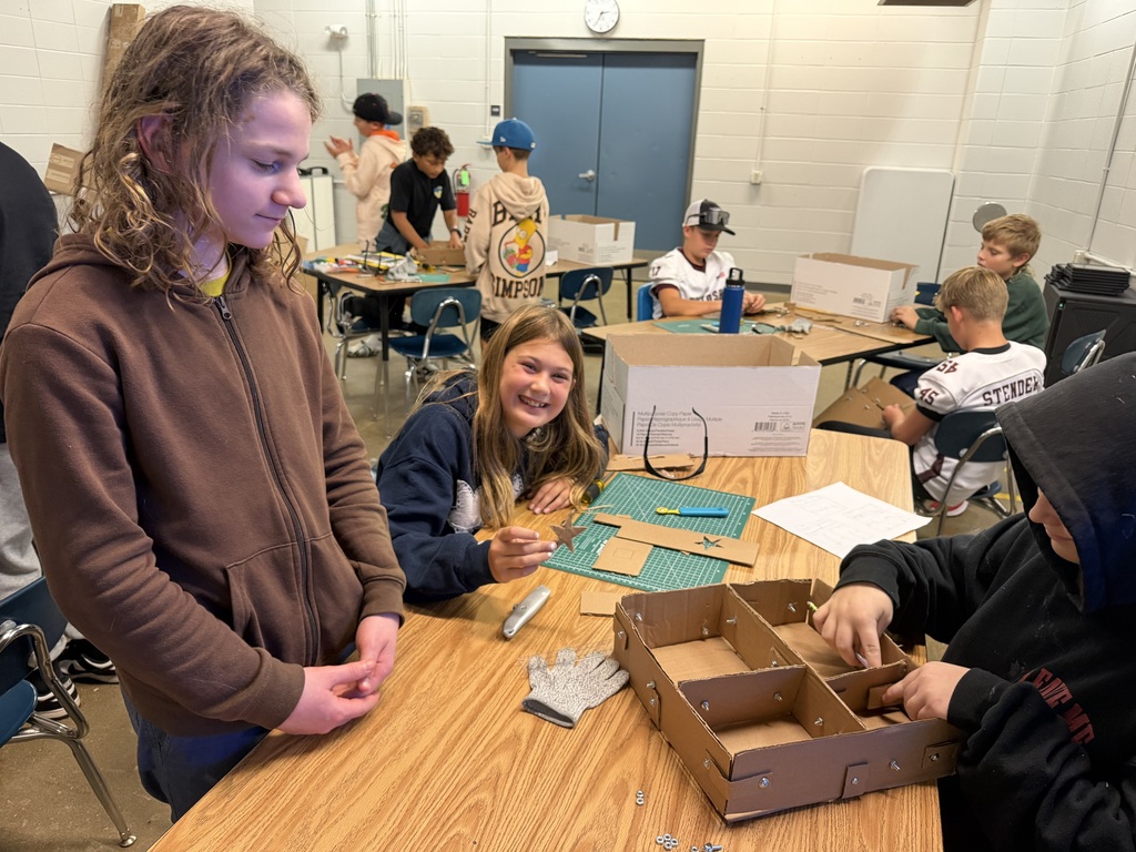 Students work together at a table building cardboard prototypes during a hands-on classroom project.