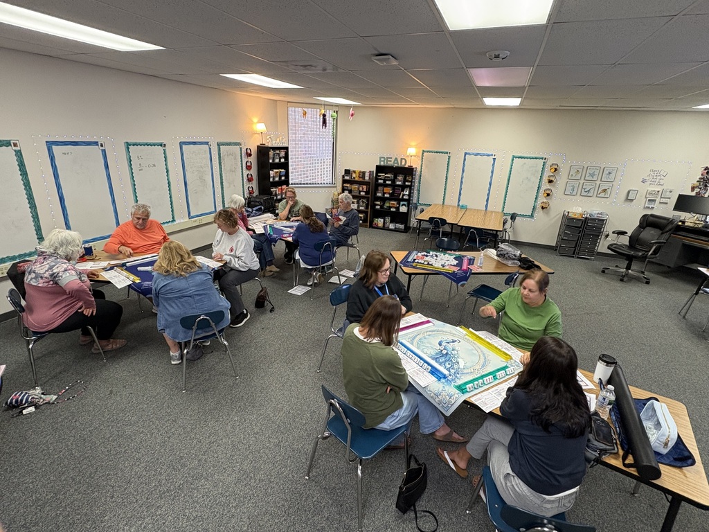 Wide view of a classroom filled with people gathered around small tables playing Mahjong together.