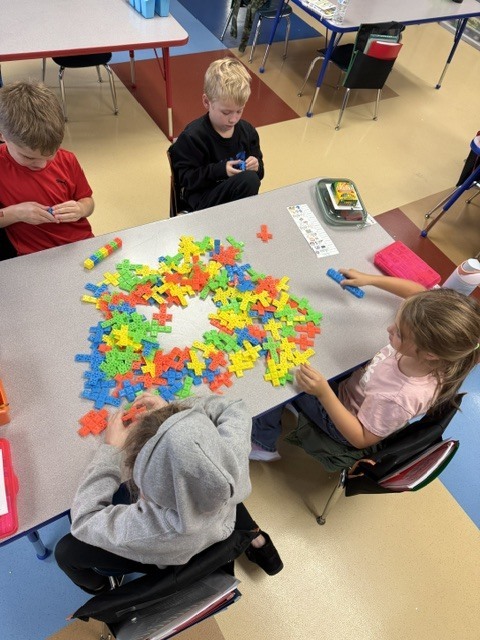 Students gathered around a classroom table building structures with colorful interlocking plastic cross blocks.