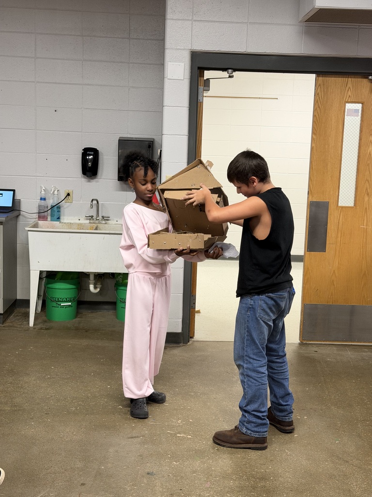 Two students work together to inspect and construct a detailed cardboard structure project.